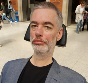 Alan Benson, a white man with grey hair and beard using a power chair