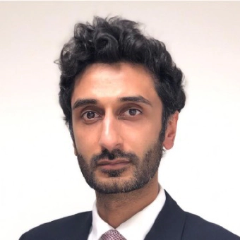 Waleed Ahmed, a man with curly black hair, and the COO of Transreport, facing the camera, wearing a dark suit with a white shirt and purple tie.