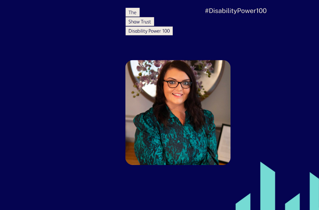 Photo of Emma Partlow, a white woman with long dark brown hair, brown glasses and a blue patterned dress. Emma is smiling in front of purple orchids. Above the photo text reads "The Shaw Trust Disability Power 100" in blue font in cream boxes, with the Disability Power 100 hashtag top right and two teal Transreport pillars bottom right. Navy blue background with cream text.   NEW