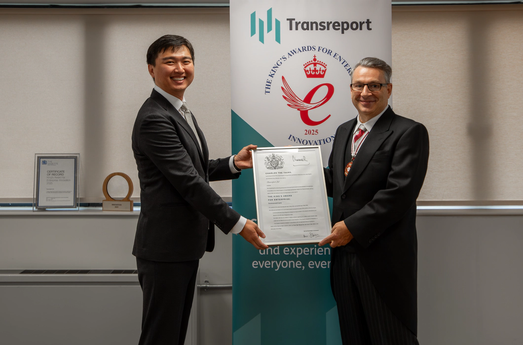 Photo of Jay Shen and Mr Kevin McGrath OBE MRICS DL smiling, holding the official King’s Award certificate together. They stand in front of the Transreport King’s Award for Enterprise in Innovation banner.