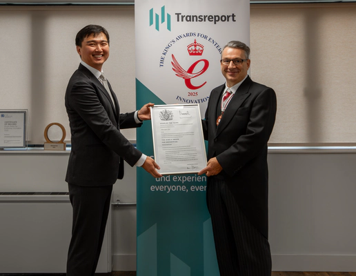 Photo of Jay Shen and Mr Kevin McGrath OBE MRICS DL smiling, holding the official King’s Award certificate together. They stand in front of the Transreport King’s Award for Enterprise in Innovation banner.