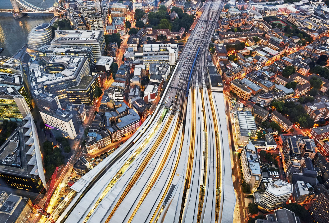 An aerial view of several trains on converging train tracks in a big city with skyscrapers.