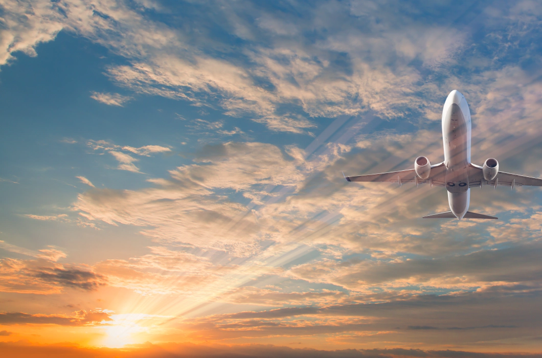 A picture of a white passenger plane from below, against a blue sky filled with clouds and a lens flare from the sun