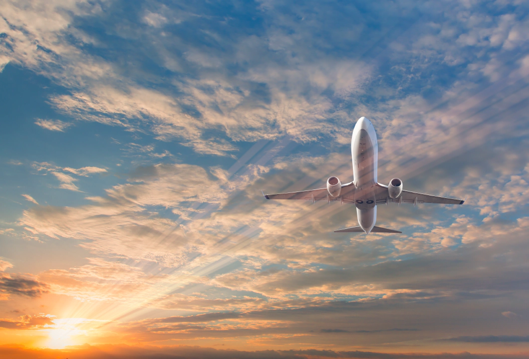 A picture of a white passenger plane from below, against a blue sky filled with clouds and a lens flare from the sun