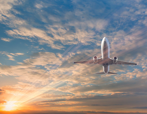 A picture of a white passenger plane from below, against a blue sky filled with clouds and a lens flare from the sun