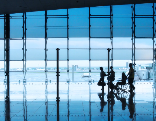 Four silhouettes of people in an airport setting, with a man and woman walking together with suitcases, followed by a wheelchair user being pushed by another person