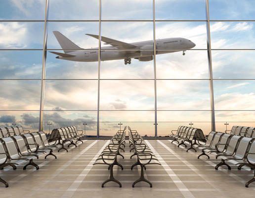 An empty airport lounge with floor to ceiling glass windows looking out onto an airport runway, with a commercial passenger aeroplane mid-take off in the background. An empty airport lounge with floor to ceiling glass windows looking out onto an airport runway, with a commercial passenger aeroplane mid-take off in the background.