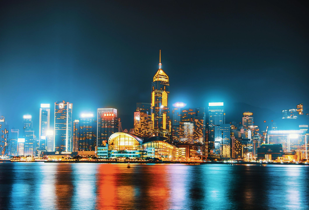 A photo of a glowing city skyline with illuminated skyscrapers at night, reflecting in a river.