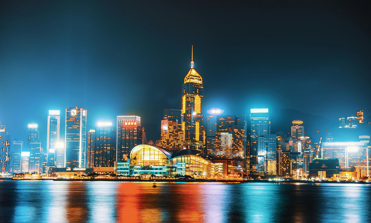 A photo of a glowing city skyline with illuminated skyscrapers at night, reflecting in a river.