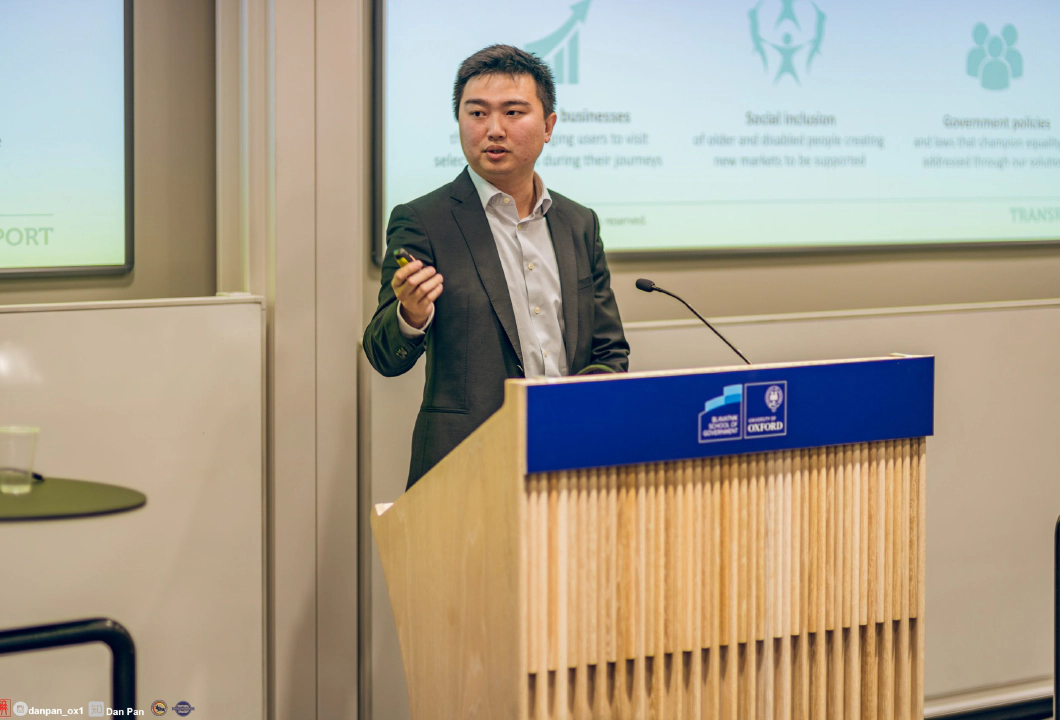 Jay Shen, an asian man with short black hair, and CEO of Transreport, in a grey suit standing at a speaking podium.
