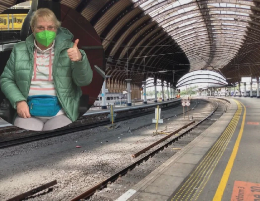 A picture of an older woman, wearing a face mask and with her thumbs up, is overlayed on top of a picture of an empty train platform