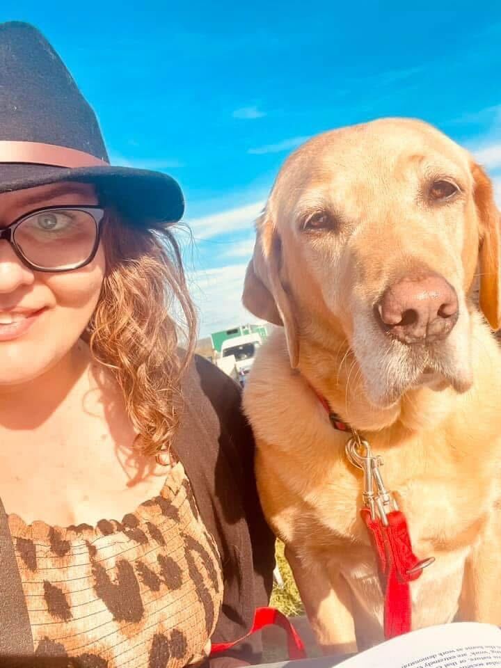 Emma with her assistance dog Luna under a bright blue sky with glowing sunlight.