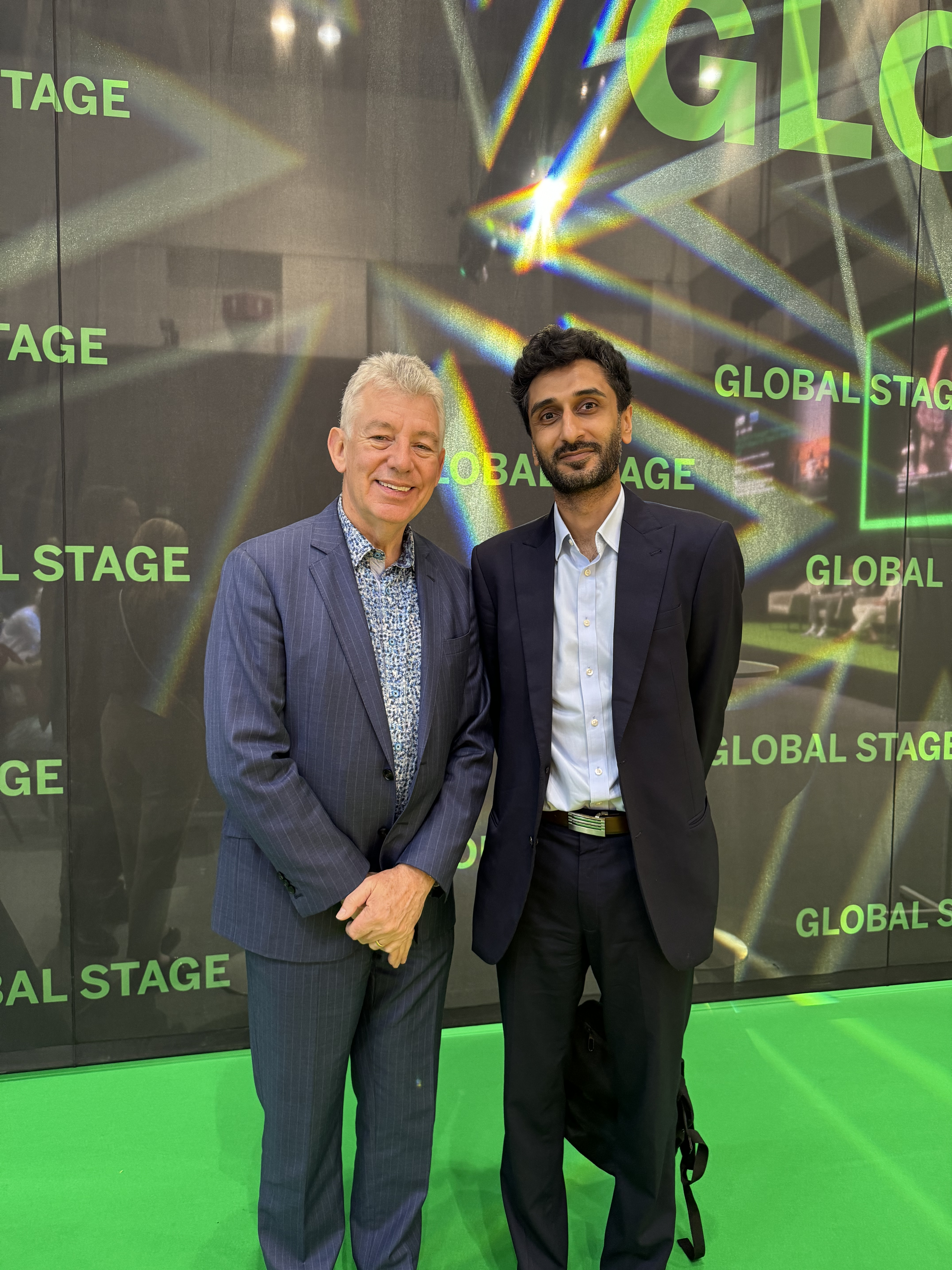 Waleed Ahmed, Transreport's COO, with Paul Griffiths, Dubai Airports CEO. They are standing together in front of the black and green Global Stage sign and smiling.