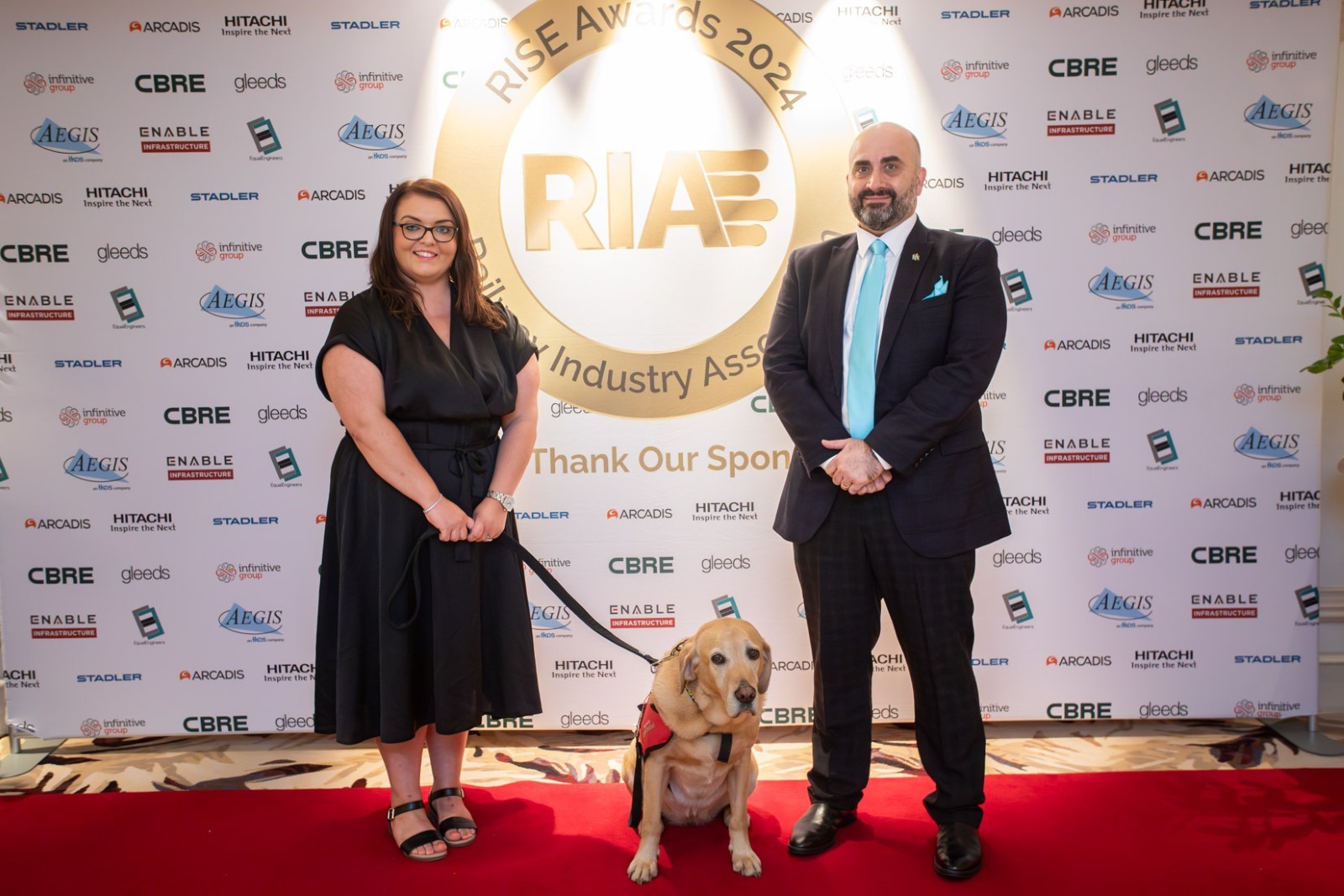 Photo of Joseph Mastracci, Commercial Manager and Emma Partlow, Accessibility and Inclusion Manager, hold Transreport's RIA RISE Award in front of the RISE Awards banner. Joseph is wearing a black suit with a white shirt and blue tie in a nod to Transreport's brand colours. Emma is wearing a black dress and holding her assistance dog Luna on a black lead. They are both smiling and the photo gives a sense of celebration and collaboration.Joseph Mastracci, Commercial Manager and Emma Partlow, Accessibility and Inclusion Manager, hold Transreport's RIA RISE Award in front of the RISE Awards banner. Joseph is wearing a black suit with a white shirt and blue tie in a nod to Transreport's brand colours. Emma is wearing a black dress and holding her assistance dog Luna on a black lead. They are both smiling and the photo gives a sense of celebration and collaboration.