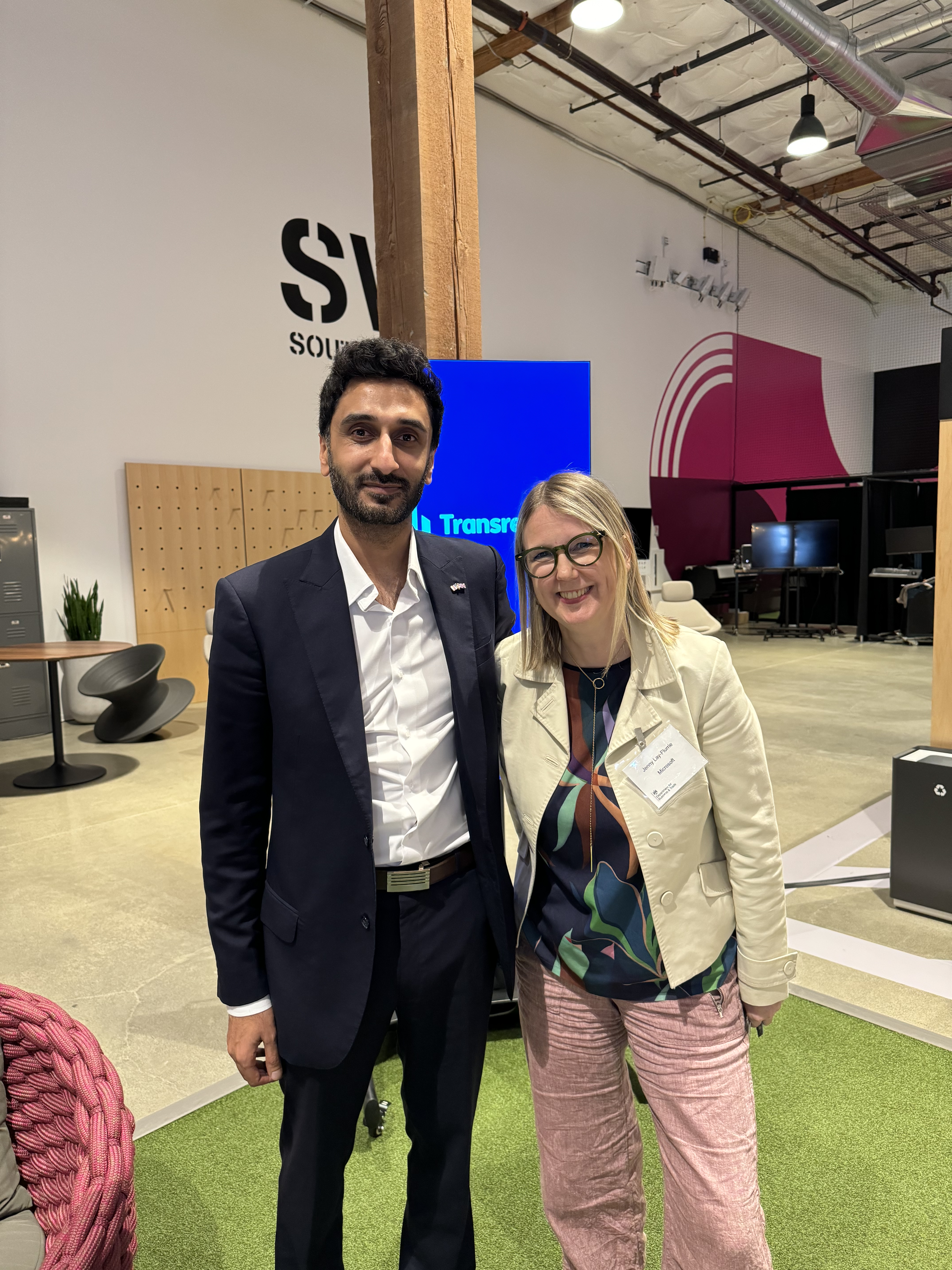 Transreport's COO Waleed Ahmed with Jenny Lay-Flurrie, Microsoft's Chief Accessibility Officer. Waleed is wearing a navy suit with a white shirt. Jenny is wearing a cream jacket and pink trousers. They are both smiling.