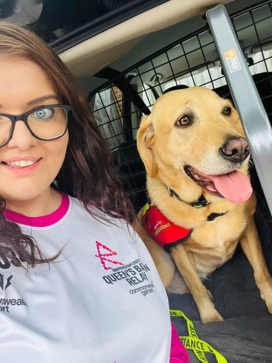 Emma Partlow, a white female and Transreport's Accessibility & Inclusion Manager, sitting beside her assistance dog Luna.