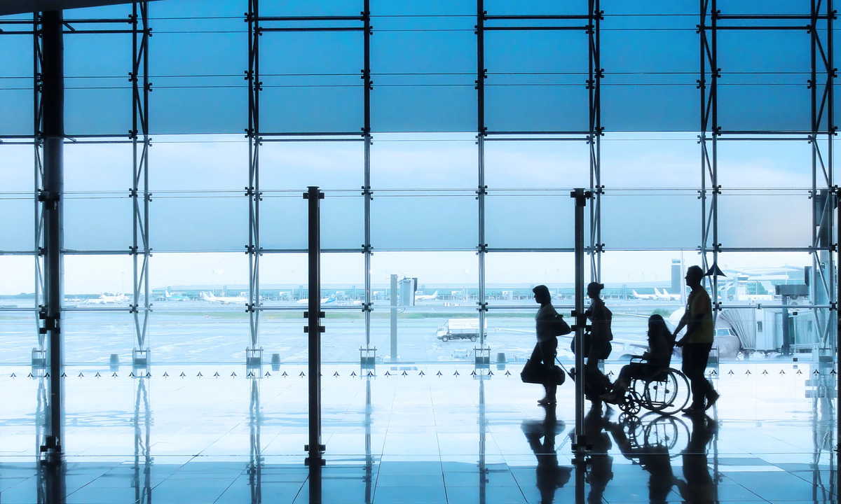 Four silhouettes of people in an airport setting, with a man and woman walking together with suitcases, followed by a wheelchair user being pushed by another person Four silhouettes of people in an airport setting, with a man and woman walking together with suitcases, followed by a wheelchair user being pushed by another person
