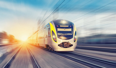 Image of a train travelling at high speed on a track with a blurred effect to convey movement and a sunset in the background.