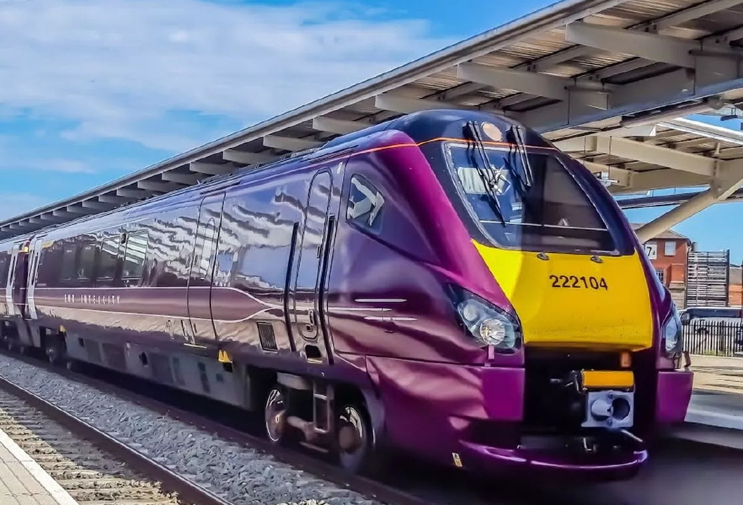 A purple and yellow East Midlands Railway train sat stationary at a train station.