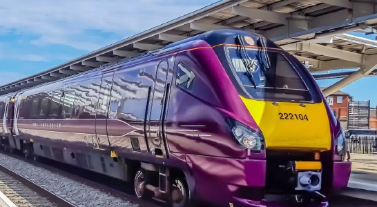 A purple and yellow East Midlands Railway train sat stationary at a train station.