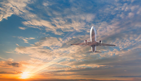 A picture of a white passenger plane from below, against a blue sky filled with clouds and a lens flare from the sun