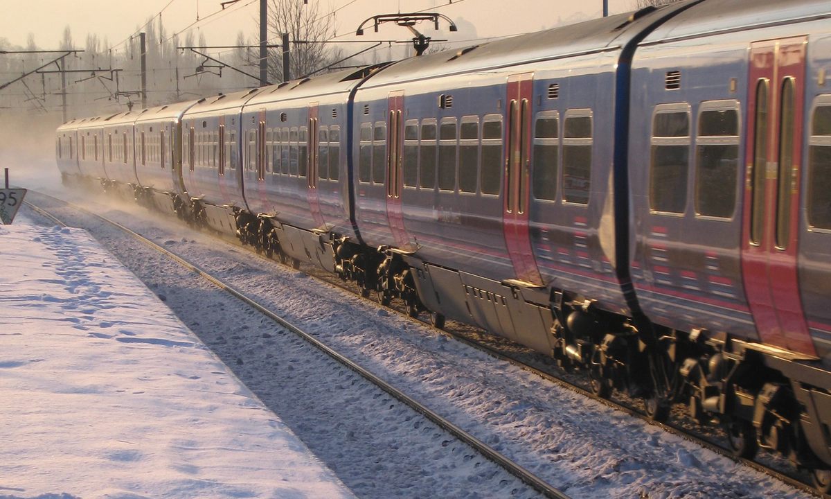 Photo of a blue and red train on a snowy track beside a snowy platform with an orange sky behind it. Photo of a blue and red train on a snowy track beside a snowy platform with an orange sky behind it.
