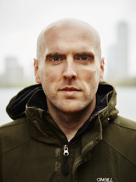 Simon Wheatcroft, a white man with a shaved head wearing a green coat and looking into the camera
