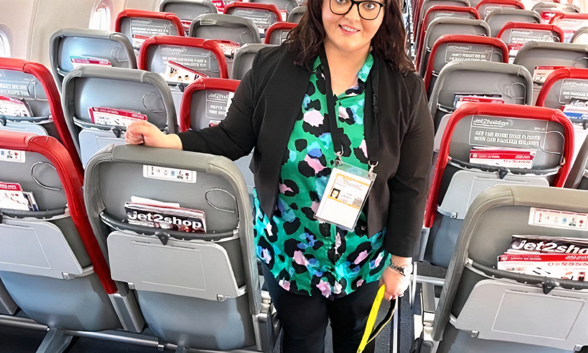 Emma Partlow, Transreport's Inclusion & Accessibility Manager, standing beside her assistance dog Luna, in the middle aisle of a commercial passenger aeroplane.
