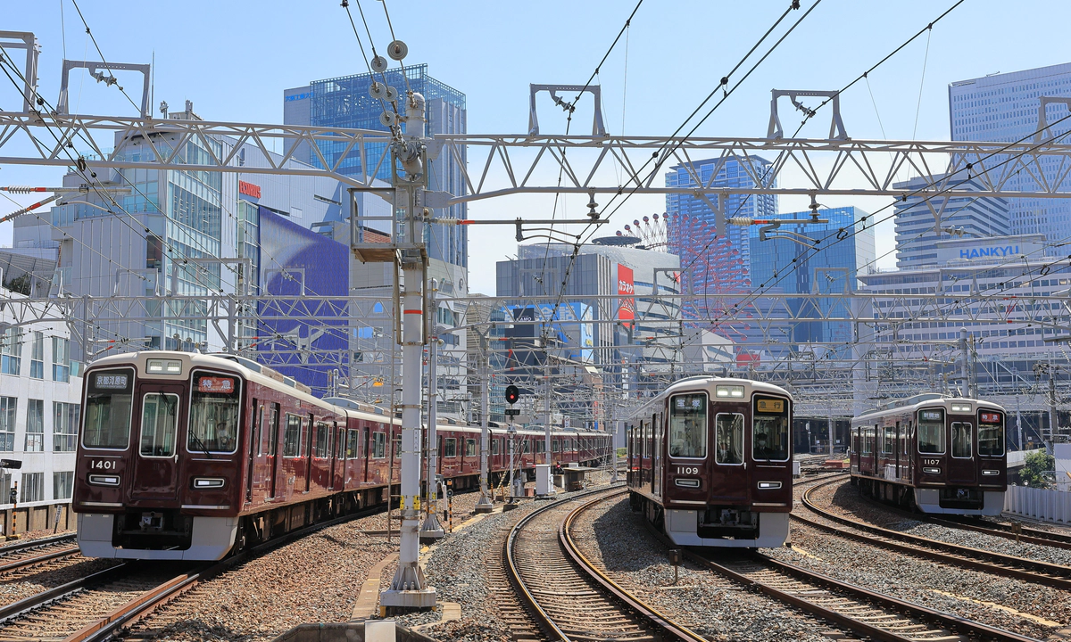 Two red trains moving along train tracks at a Japanese train station.