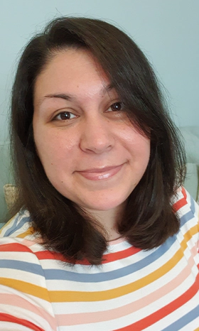 Victoria, a woman with long, dark hair wearing a white top with red, blue, yellow, and pink horizontal stripes across it, smiling at the camera.